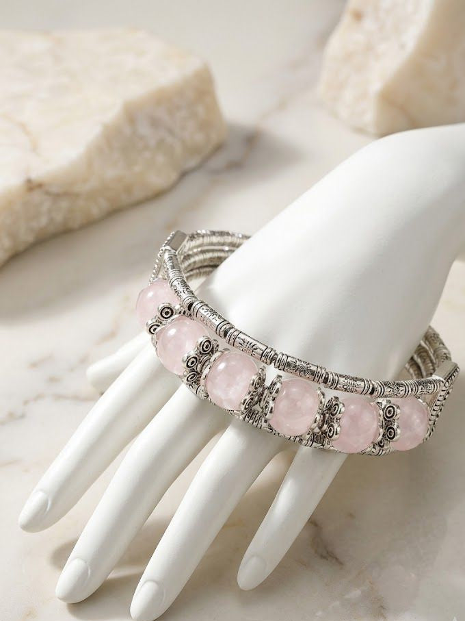 A silver-toned bohemian-style cuff bracelet with large oval pink stones, displayed on a white ceramic mannequin hand over a light marble surface.