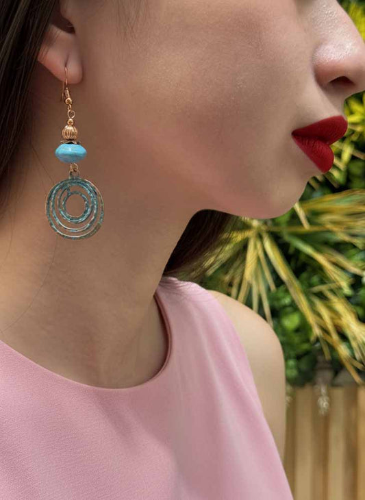 Close-up of a woman wearing a turquoise earring with a gold accent, set against a blurred green background.