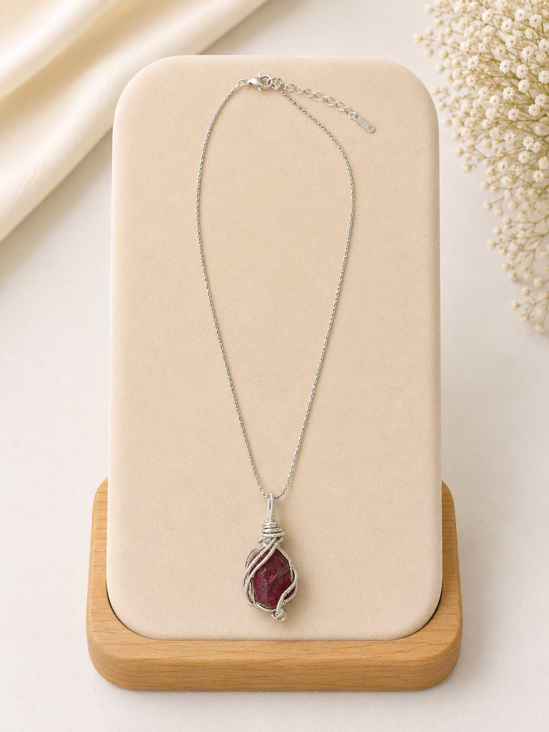 Silver necklace with a red pendant on a beige display stand.