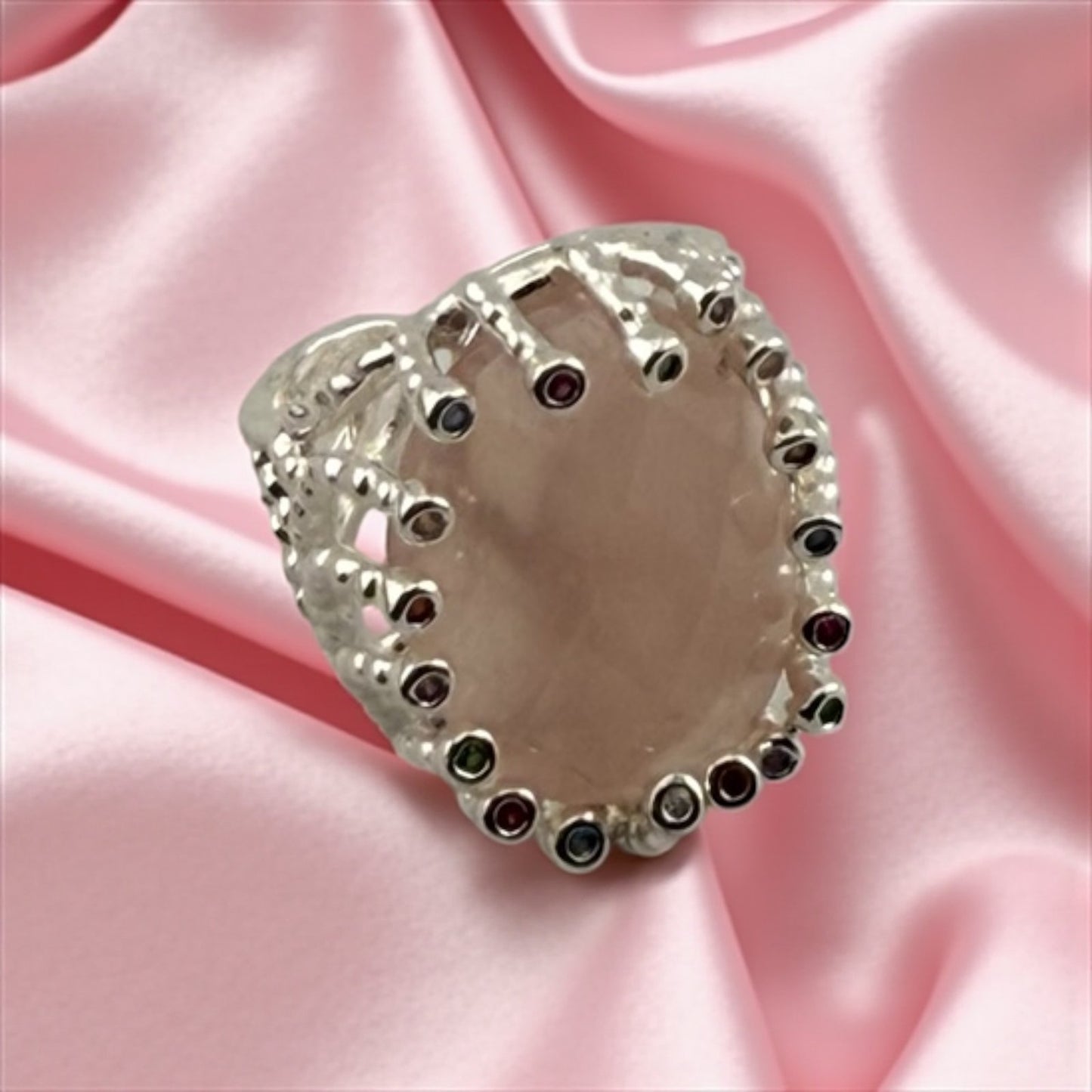 Heart-shaped silver ring with embedded stones on a pink satin background