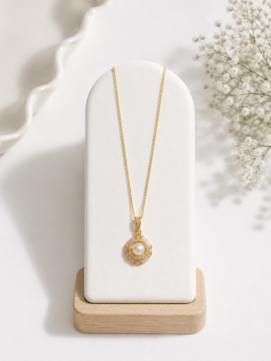Gold necklace with a pearl pendant on a white stand with a soft background