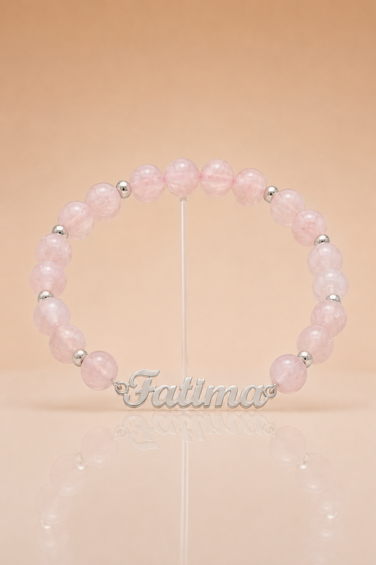 Pink beaded bracelet with silver name charm on a beige background