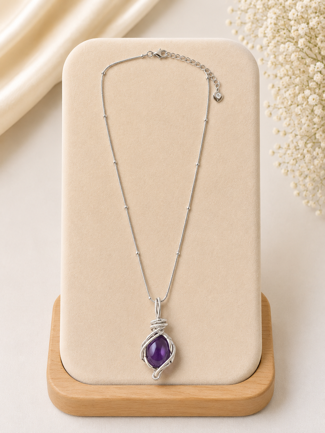 Silver necklace with a purple pendant on a beige stand with a light background