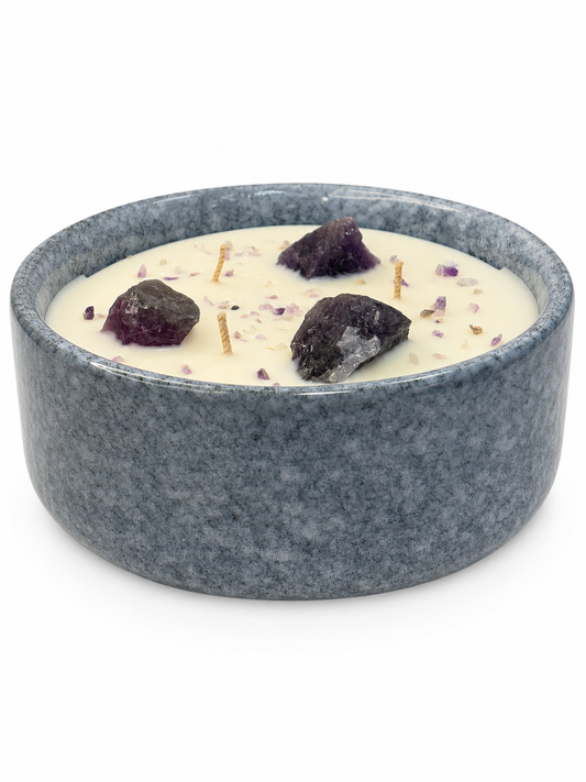 Candle in a gray ceramic bowl with dark purple stones on a white background