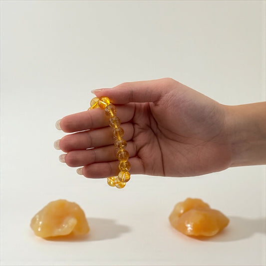 Hand holding a yellow beaded bracelet with two yellow objects on a white background