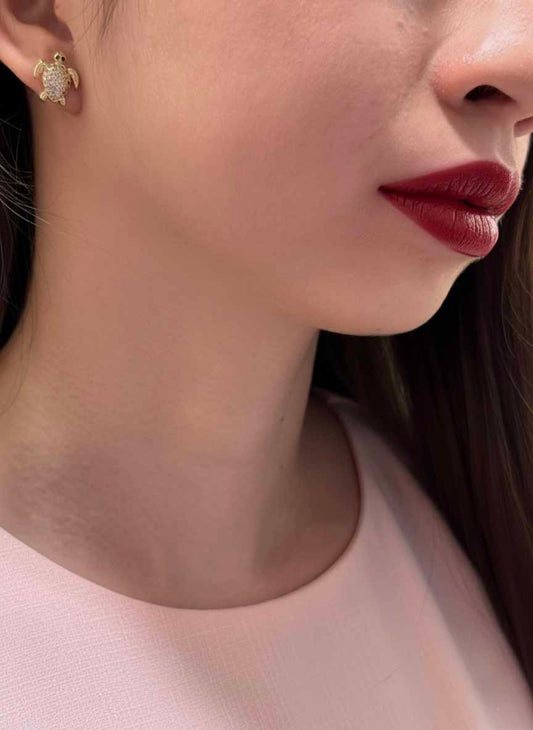 Close-up of a person wearing turtle-shaped earrings with a soft pink top.