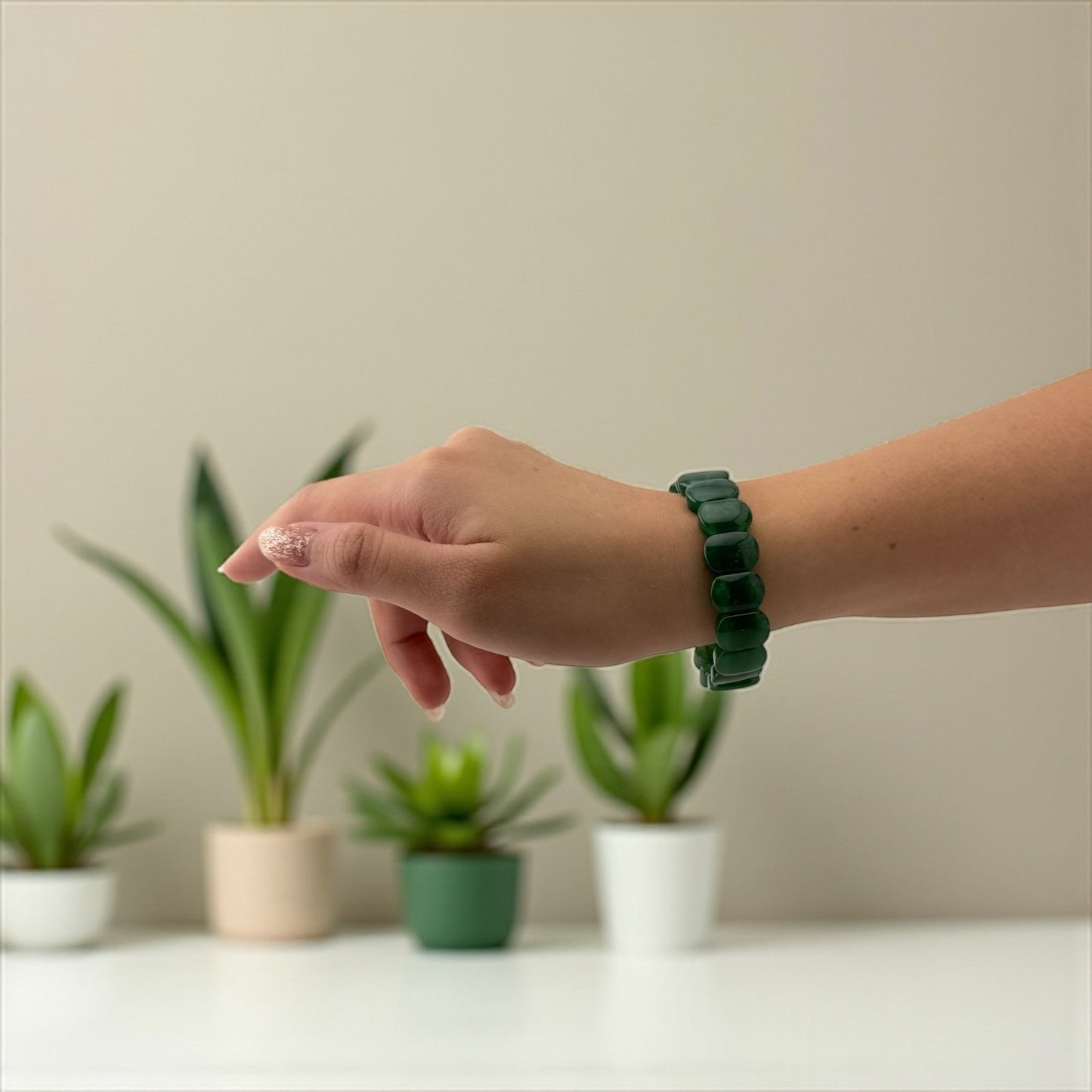 Hand wearing a green bracelet with plants in the background