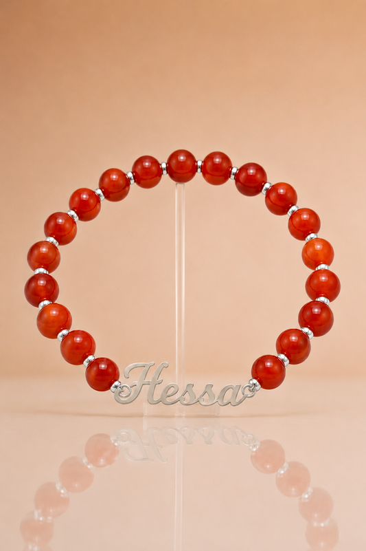 Red beaded bracelet with silver accents on a beige background, featuring the brand 'Hessa'.