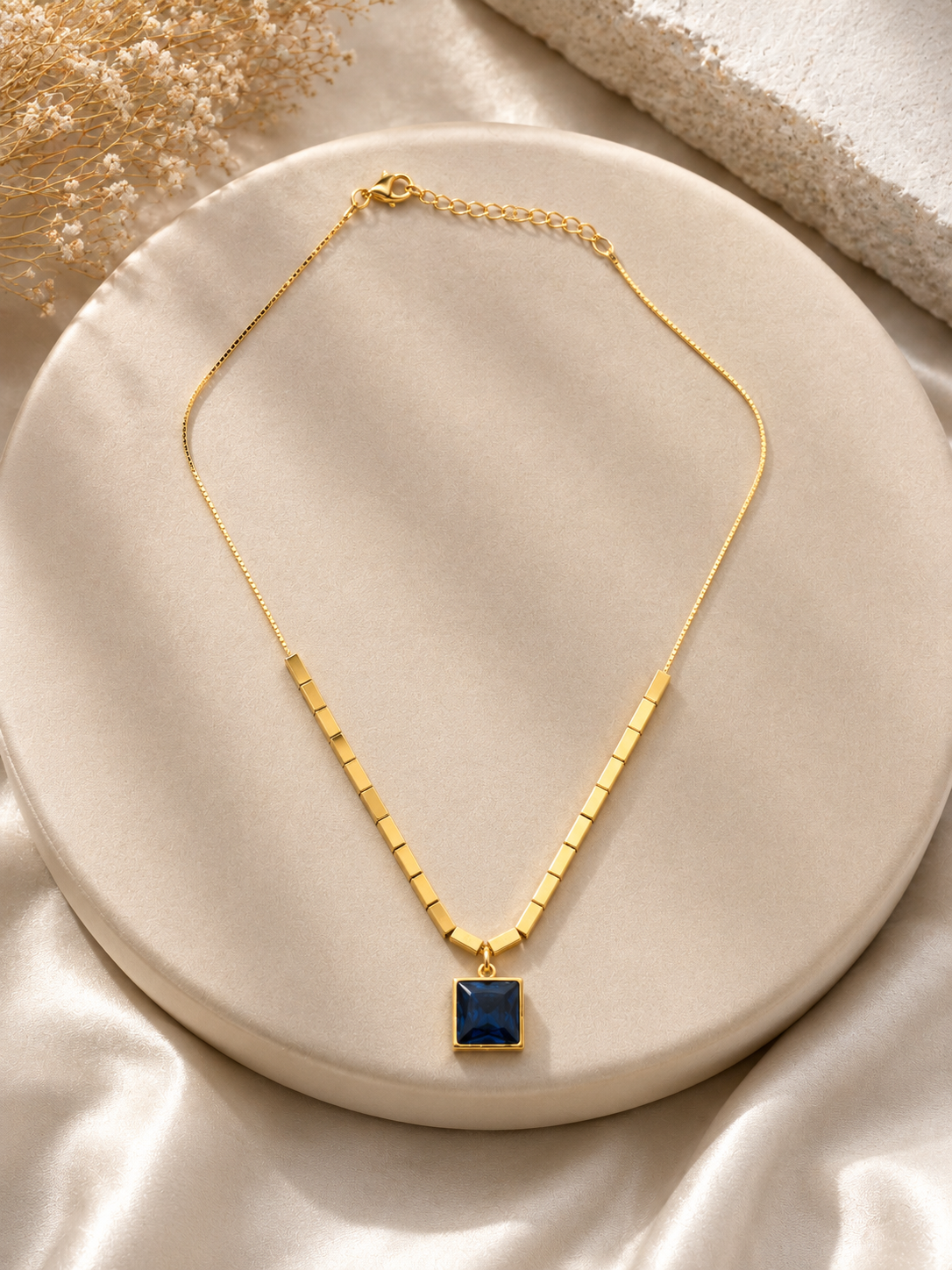 Gold necklace with a blue pendant on a beige plate