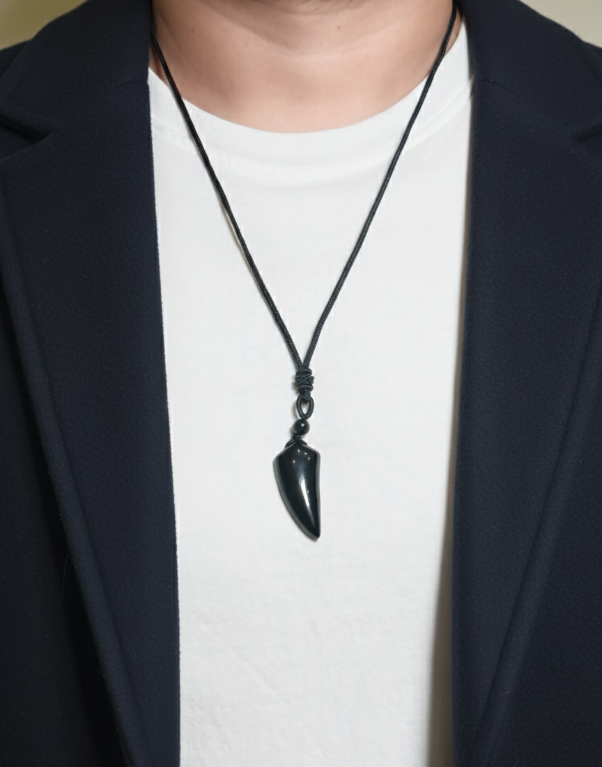 Person wearing a black necklace with a pendant against a neutral background