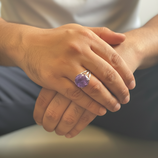 Hand wearing a ring with a purple gemstone, blurred background