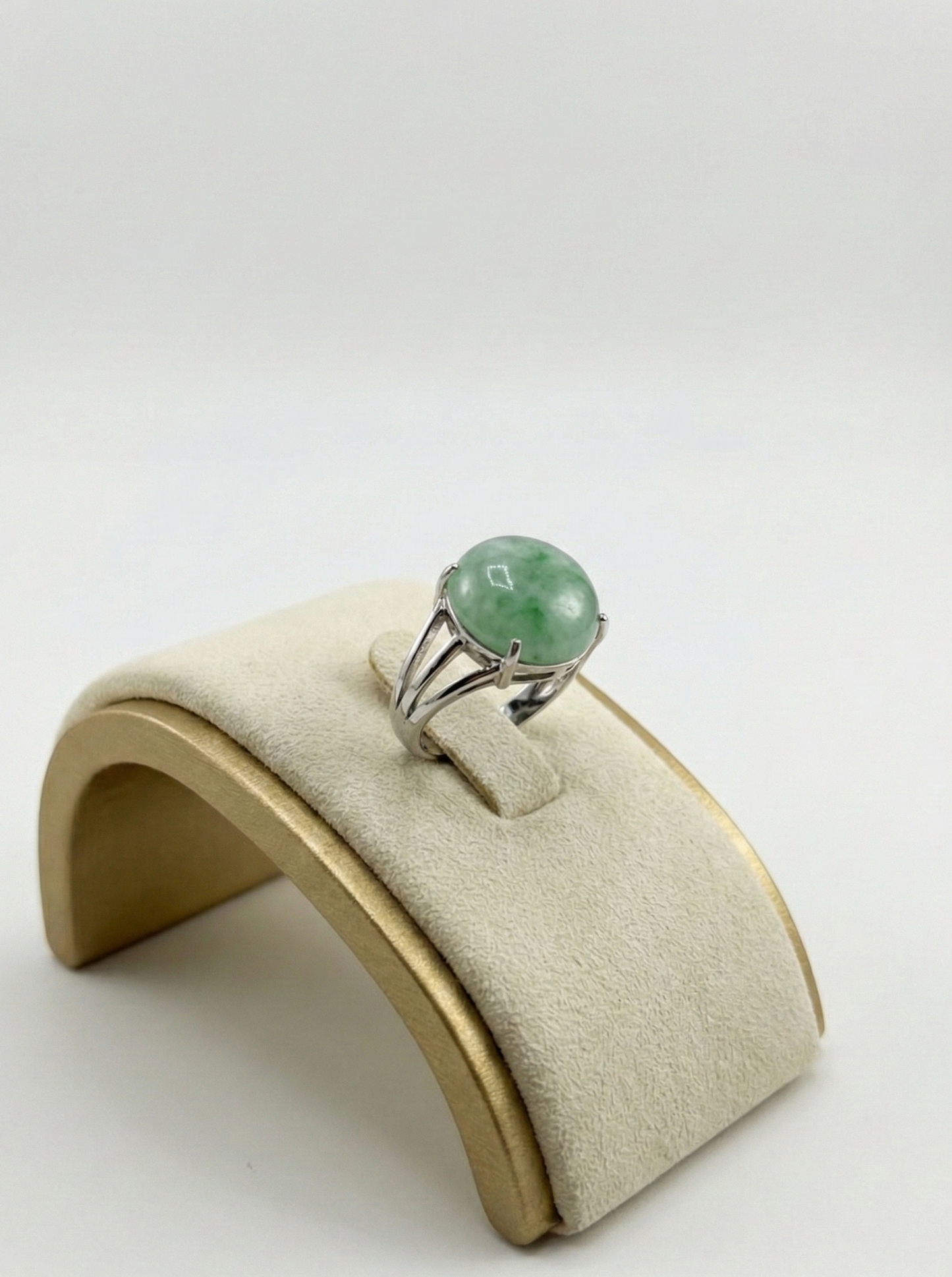 Silver ring with a green gemstone on a beige jewelry display stand against a white background