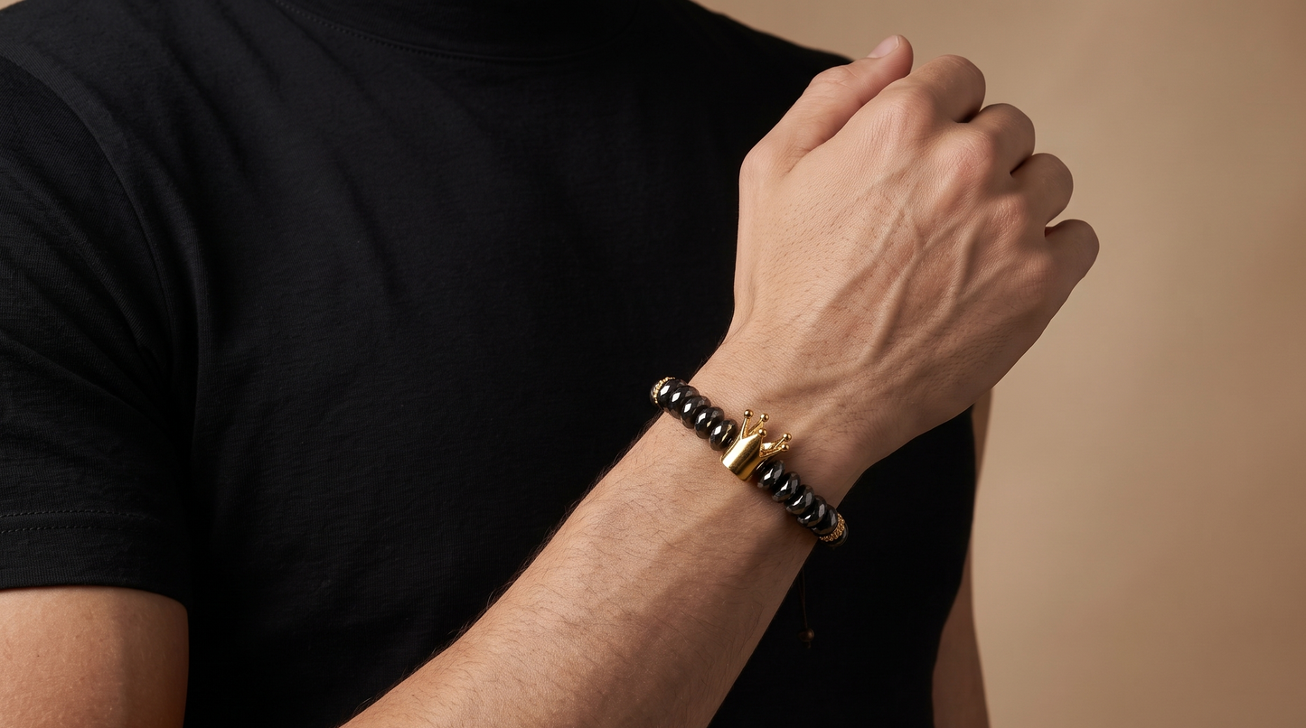A close-up of a man's arm and hand wearing a black beaded bracelet with a gold-toned tiger-head charm, set against a solid beige background.