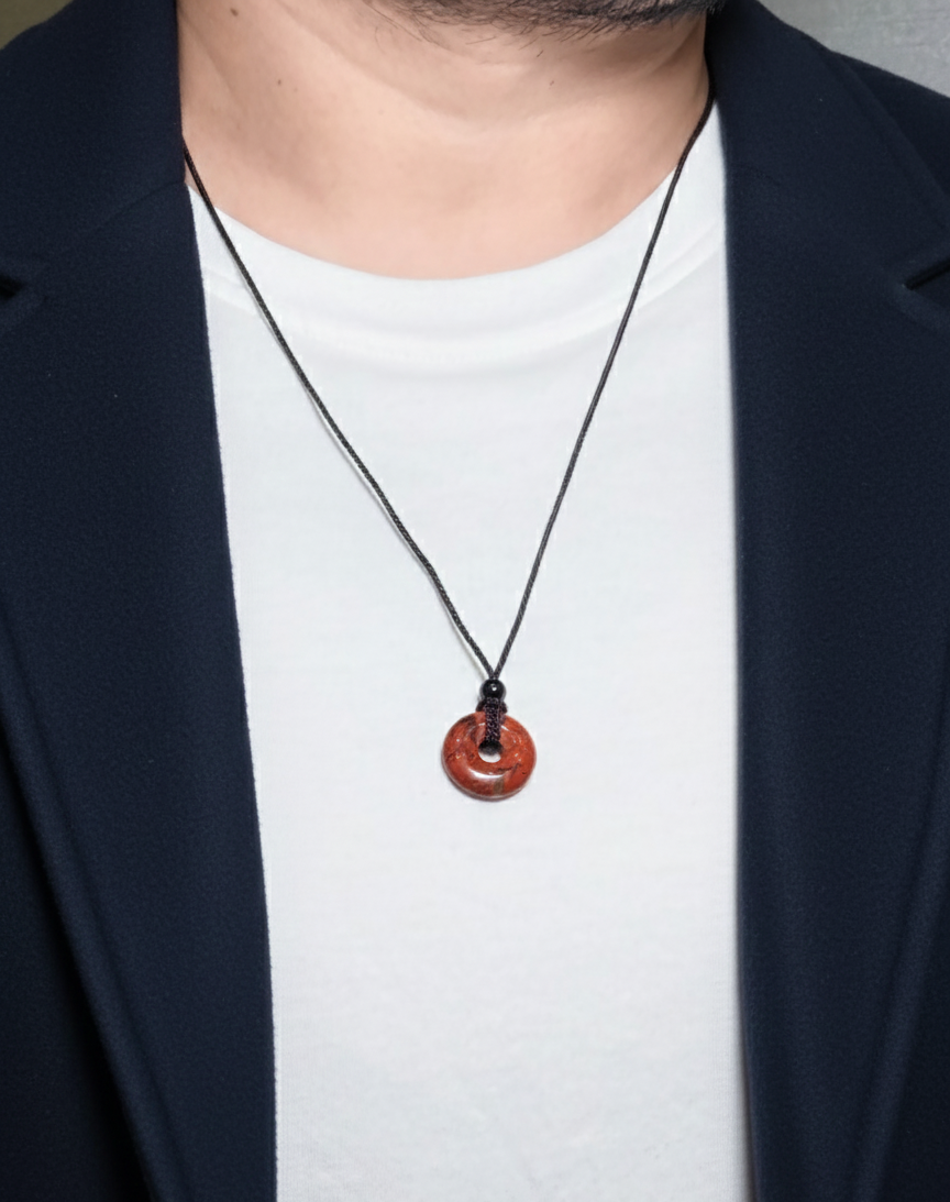 Person wearing a necklace with a red pendant on a plain background