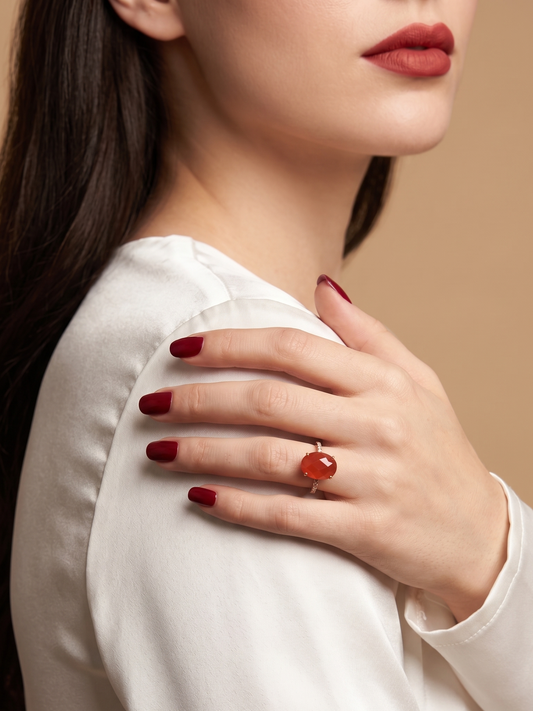 A close-up lifestyle shot of a woman wearing a silver ring with a round orange-red cabochon gemstone, resting on her shoulder.