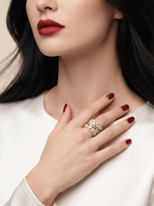 A close-up lifestyle shot of a woman wearing a textured silver ring on her finger, dressed in a white satin top against a soft beige background.