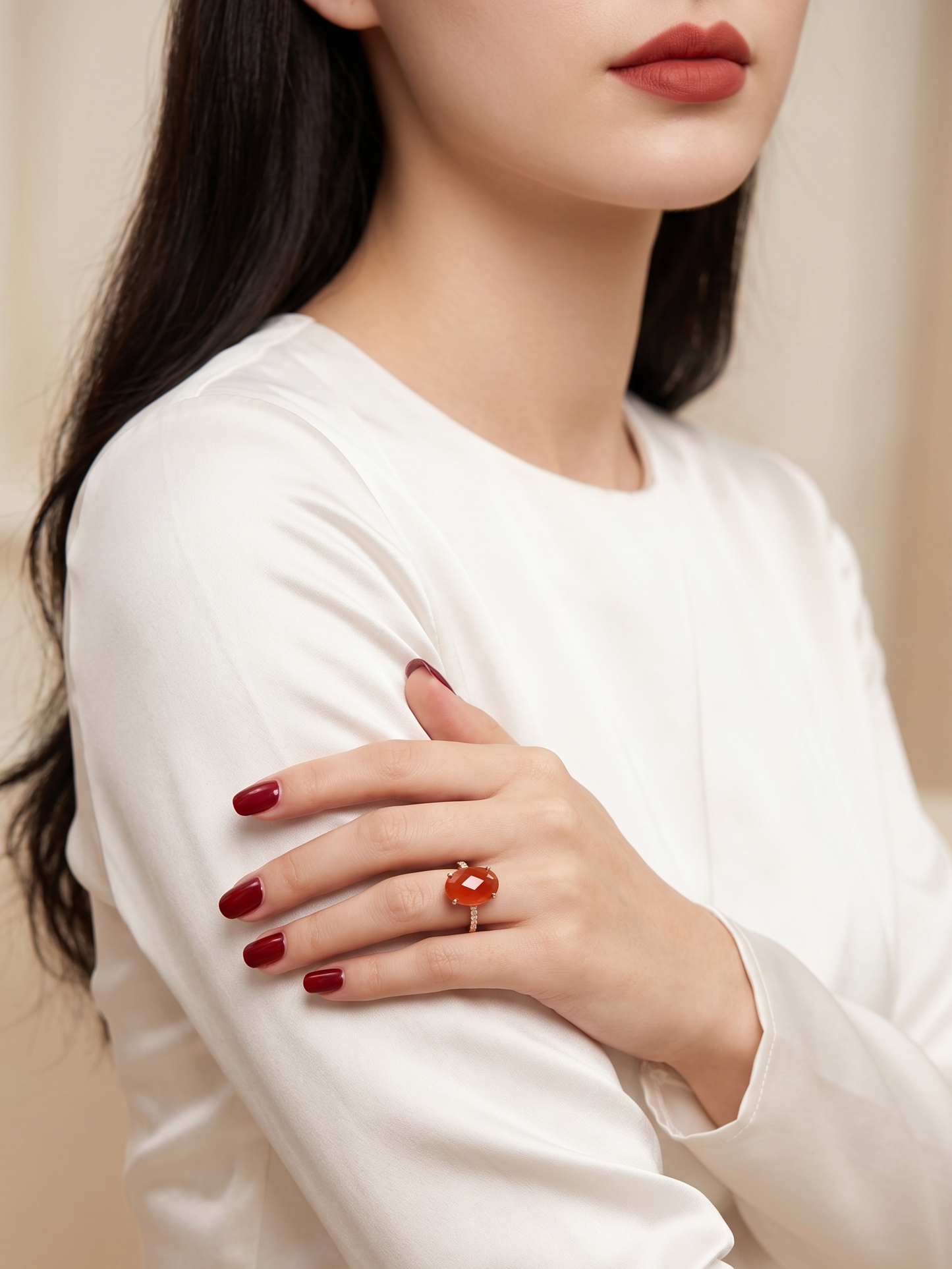 A close-up lifestyle shot of a woman wearing a gold ring with a red heart-shaped stone, styled with a white satin long-sleeve top.