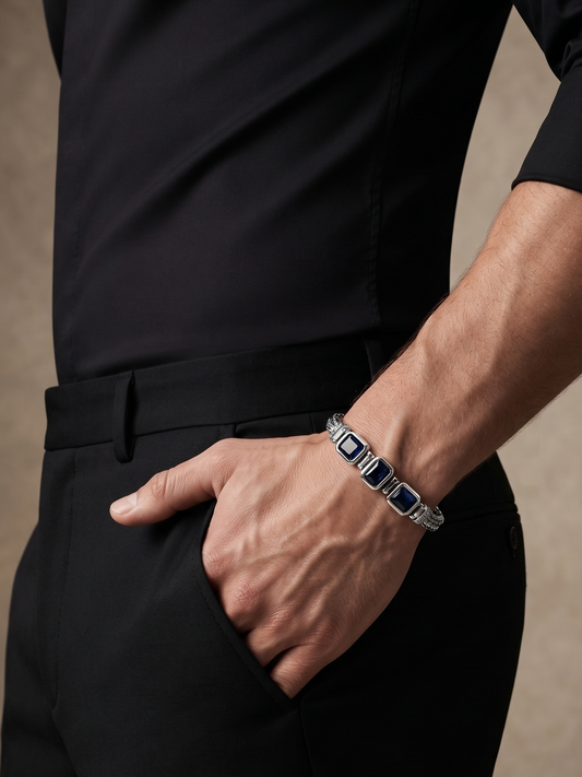 A close-up lifestyle shot of a man wearing a black shirt and trousers, showcasing a silver-toned bracelet with rectangular dark blue inlays on his wrist.