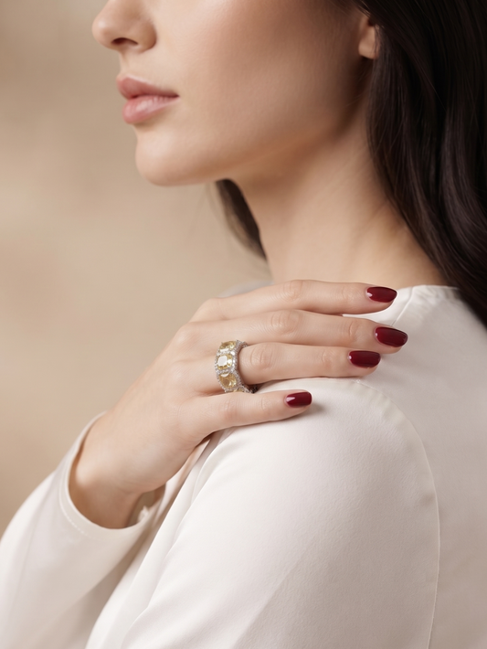 A close-up lifestyle shot of a woman wearing a silver ring with clear stones on her finger, dressed in a white satin blouse against a soft beige background.