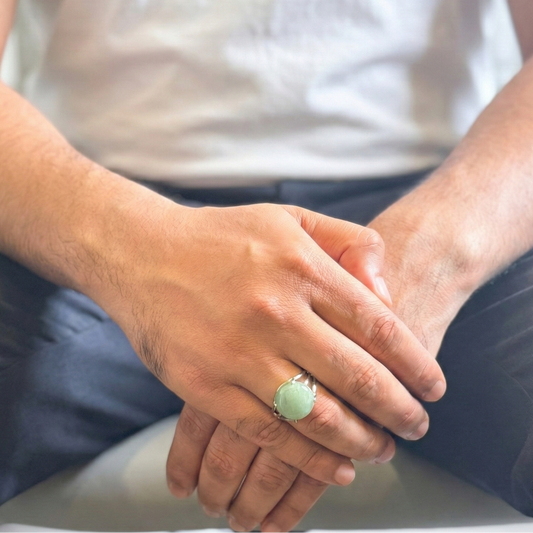 Person wearing a green ring with hands clasped together on a blurred background