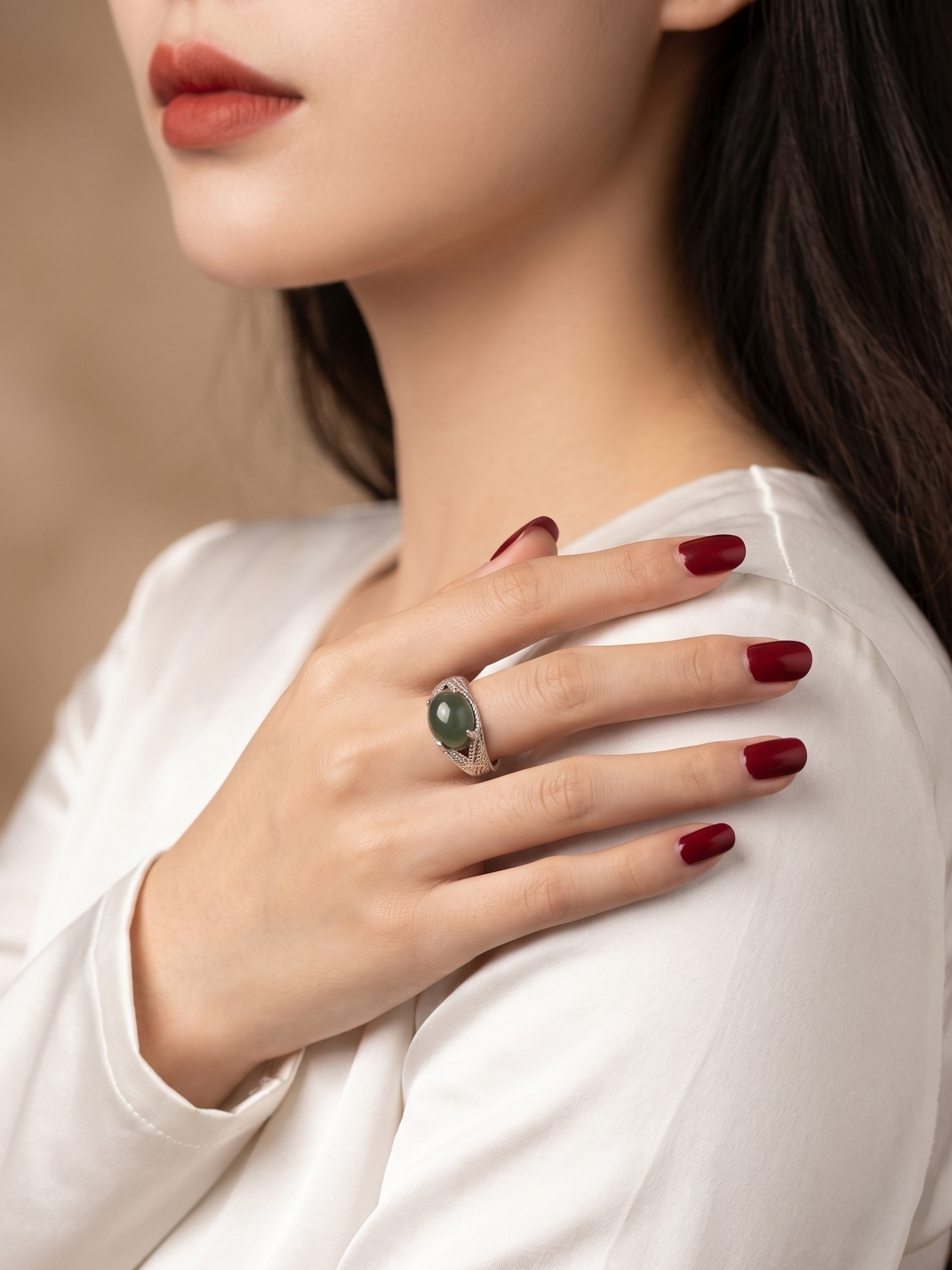 A close-up lifestyle shot of a woman wearing a silver ring with a green oval stone, resting her hand on her shoulder.