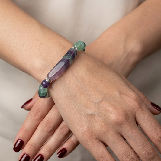 Close-up of a hand wearing a colorful beaded bracelet on a neutral background