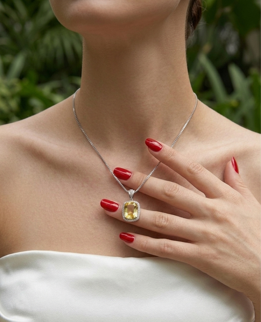 Woman wearing a silver necklace with a yellow gemstone, holding her hand to her chest.
