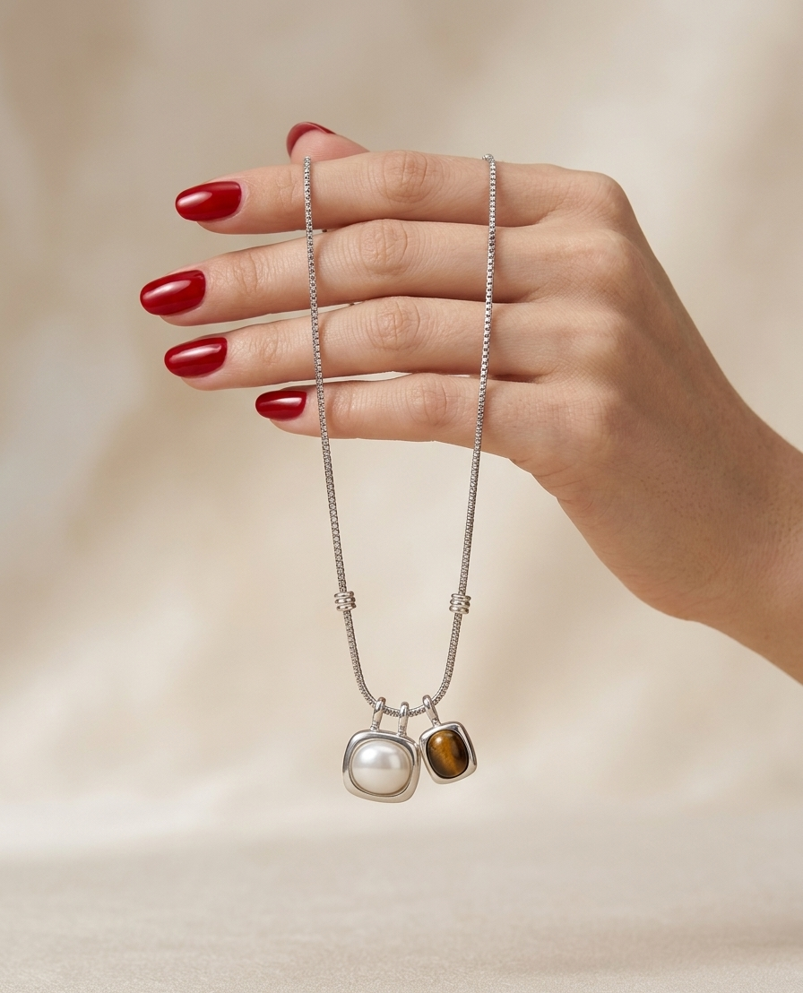 Hand wearing a necklace with two pendants against a beige background