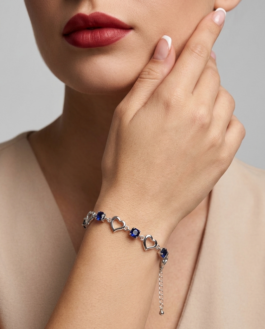 Bracelet with heart and sapphire designs worn by a person, against a neutral background