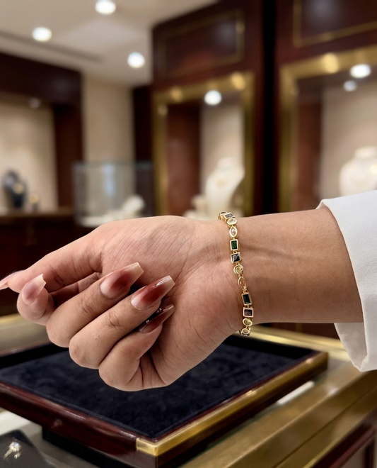 Hand wearing a gold bracelet with green gemstones in a jewelry store setting