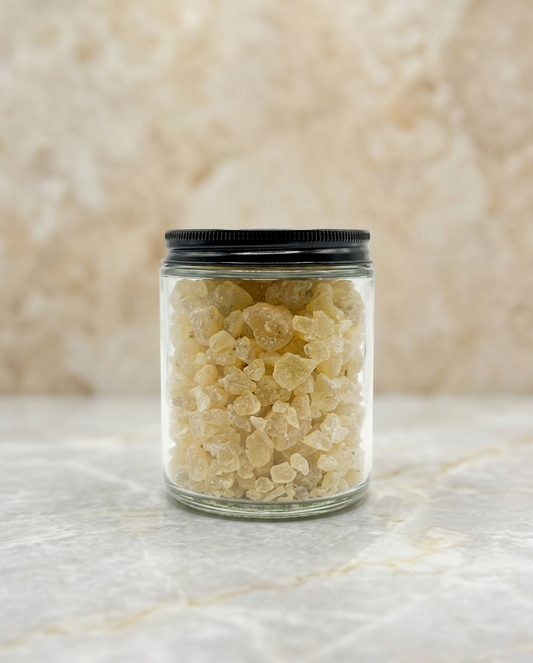 Clear glass jar with black lid containing a light-colored substance on a marble surface.