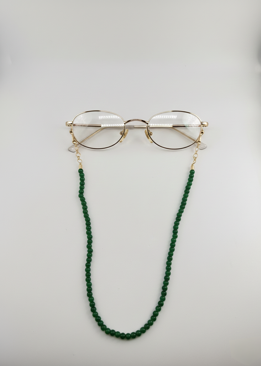 Gold-framed glasses with a green beaded chain on a light gray background