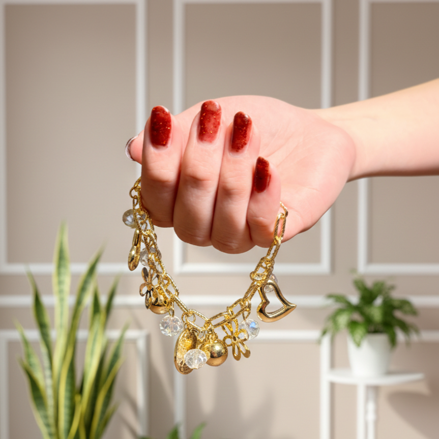 Hand holding a gold bracelet with charms against a neutral wall.
