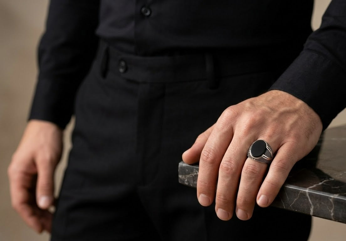 A close-up of a man's hand resting on a dark marble surface, wearing a silver-toned signet ring with a black oval face and a polished band.