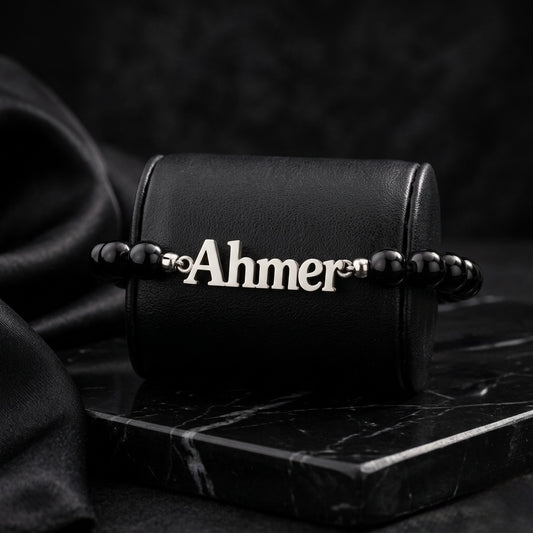 Black beaded bracelet with 'Ahmer' charm on a dark surface