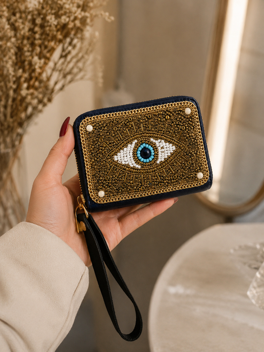 Hand holding a decorative clutch with an eye design against a neutral background