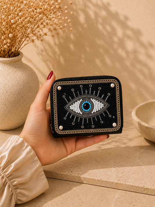 Hand holding a black wallet with eye design against a beige background