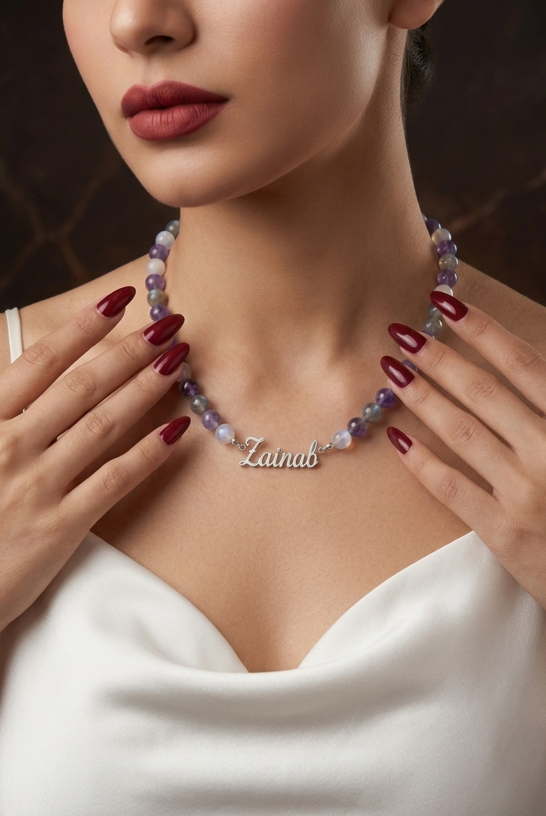 Woman wearing a necklace with 'Zainab' engraved, against a dark background