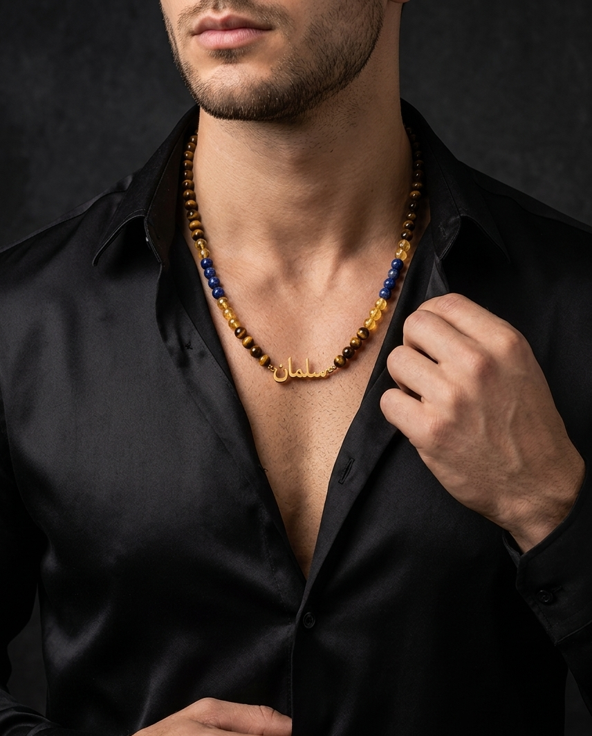 Man wearing a black shirt with an open collar, revealing a necklace with blue and gold beads.
