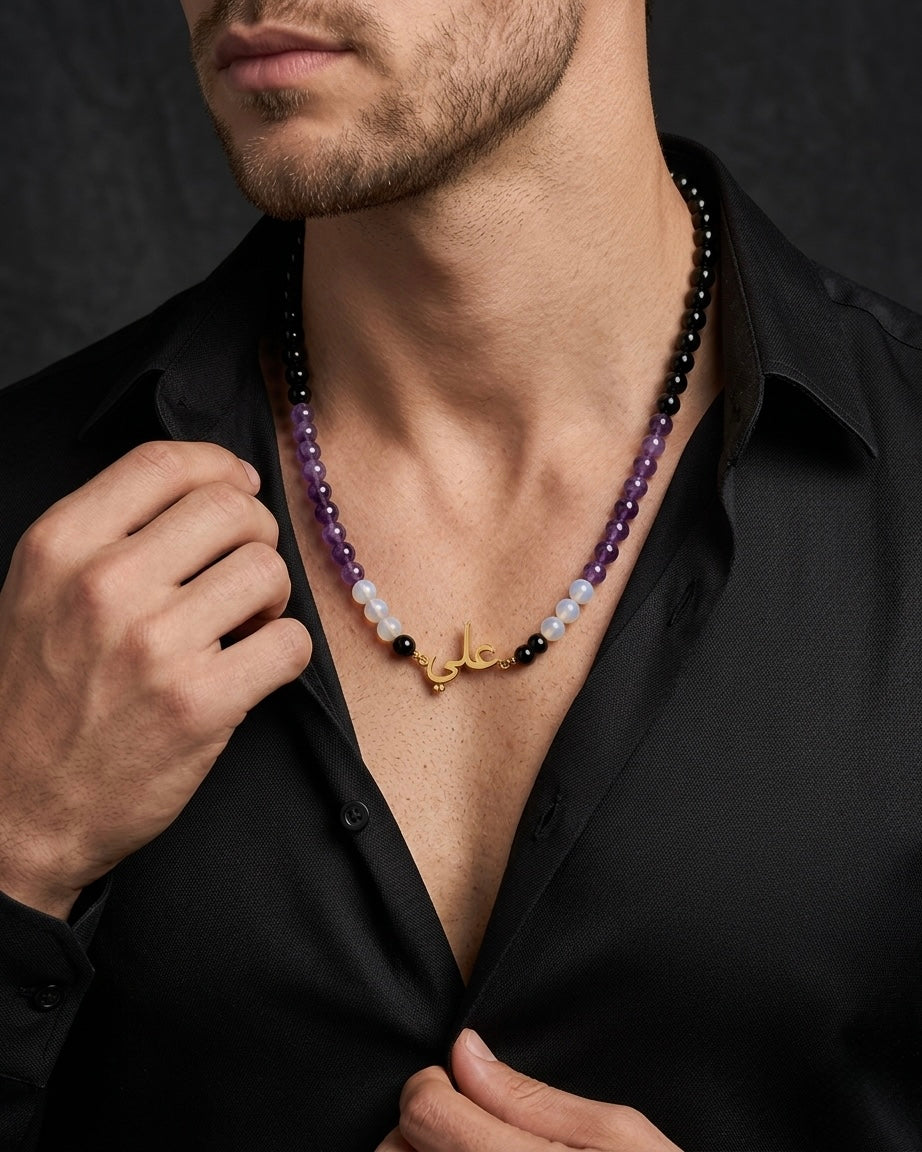 Man wearing a black shirt with a colorful beaded necklace and gold nameplate.