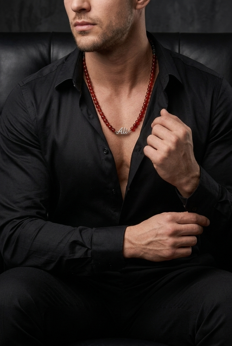 Man wearing a black shirt with a red beaded necklace, sitting on a dark leather couch.