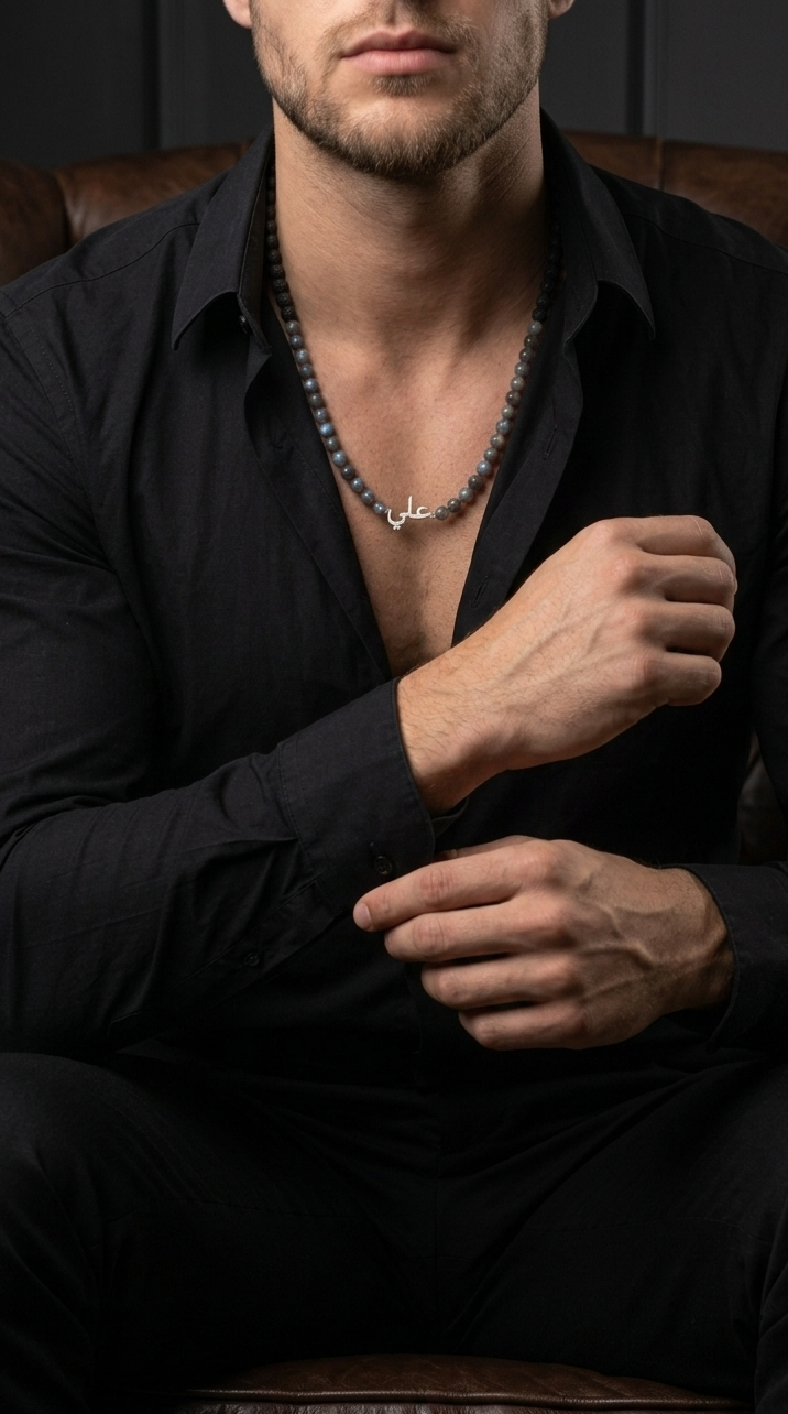 Man wearing a black shirt and necklace, sitting on a leather couch.