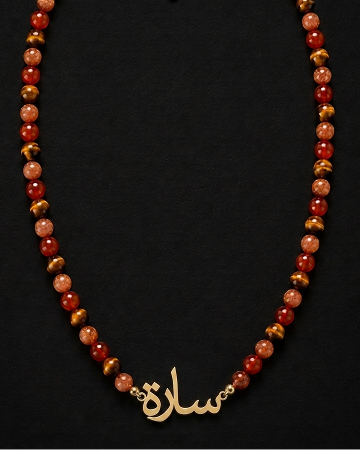Necklace with red and gold beads and a gold nameplate on a black background