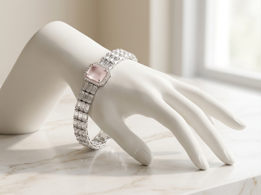 A silver-toned bracelet with a large rectangular pink gemstone and pavé-set clear stones, displayed on a white mannequin hand on a light marble surface.