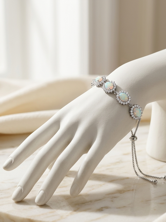 A delicate silver bracelet with three round iridescent opal-like centers and surrounding clear stones, displayed on a white mannequin hand over a light marble surface.