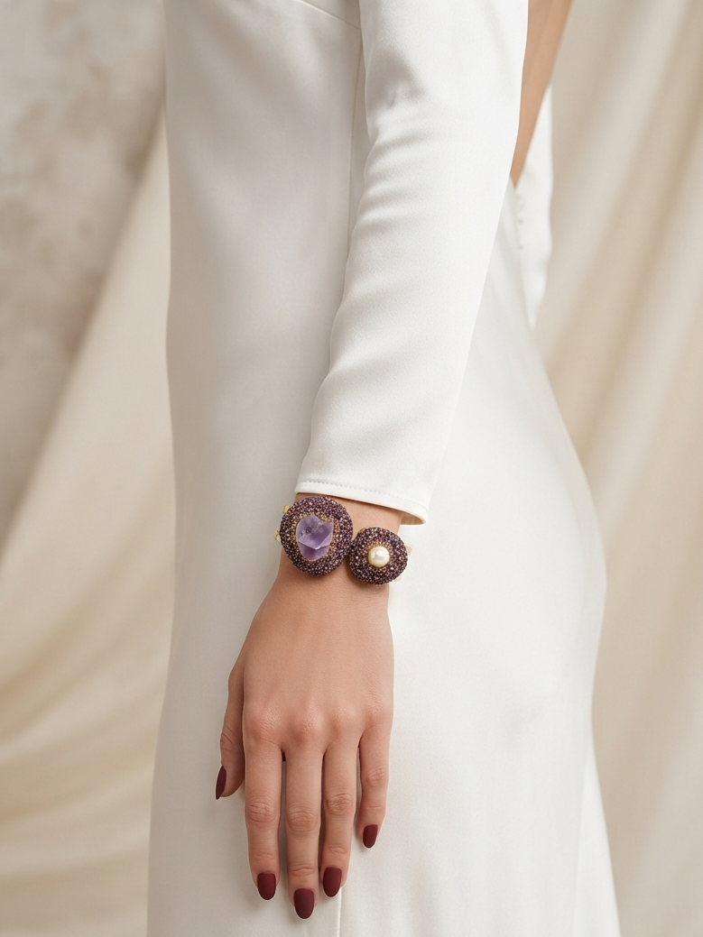 A close-up of a person wearing a white long-sleeve dress, showcasing a unique woven bracelet with purple and brown circular patterns on their wrist.