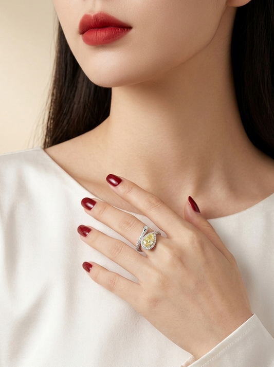 A close-up lifestyle shot of a woman wearing a silver ring with a yellow and white stone, styled with dark red nail polish and a white satin top.
