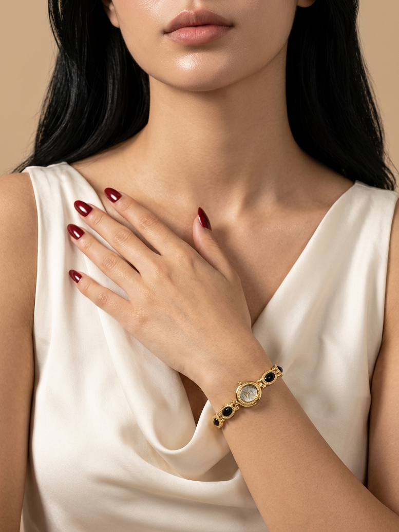 A close-up of a woman wearing a gold-toned bracelet with black and white accents, paired with a cream-colored satin top against a warm beige background.