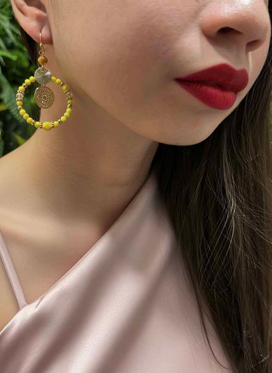 Close-up of a person wearing yellow beaded earrings with a neutral background