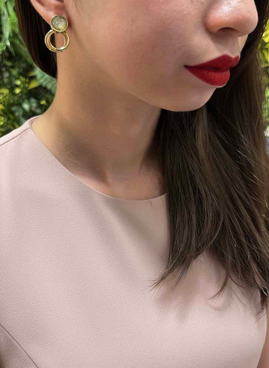 Close-up of a person wearing gold earrings with a blurred natural background